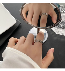 Dettaglio di un anello aperto in argento con scritta love corsiva indossato al dito