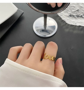Dettaglio dell'anello dorato con scritta 'love' indossato sulla mano con riflesso