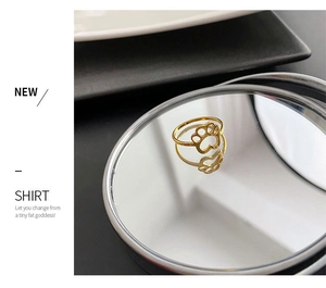 Macro detail of gold cat paw ring with heart-shaped pad on reflective mirror