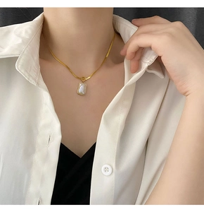 Close-up of gold blade chain with rectangular white shell pendant on a model