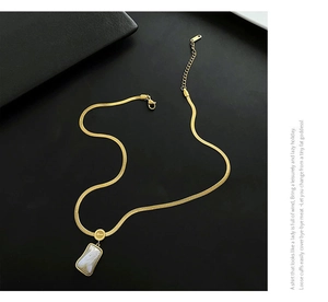 Close-up of gold-plated blade chain necklace with rectangular shell pendant on black leather