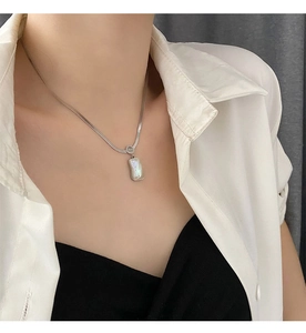 Detail of silver snake chain necklace with rectangular iridescent shell pendant on model