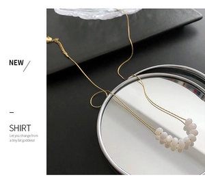 Detail of beaded pearl necklace with gold chain and white round charms on dark display