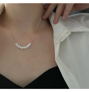 Close-up of elegant gold beaded necklace with nine white pearls on a model wearing a white shirt