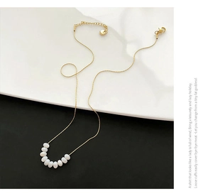 Detail of a minimalist gold necklace featuring seven white beads on a delicate chain link