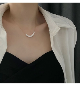 Close-up of minimalist gold chain necklace with white beads on model neck