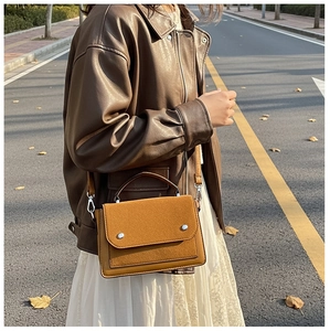 Street style view of a mustard yellow crossbody bag styled with a brown faux leather jacket
