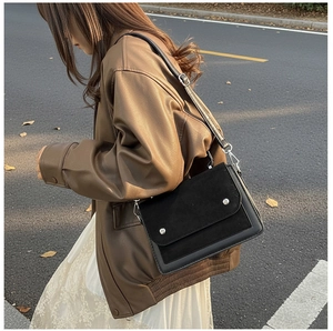 Close-up of a black leather crossbody bag featuring mixed textures and silver studs