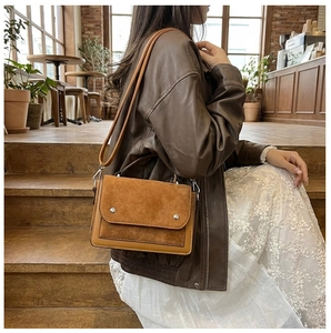 Close-up of contrast stitching texture on brown suede and leather crossbody bag detail