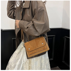 Close-up of brown suede and leather crossbody bag with silver buckle and metal chain detail