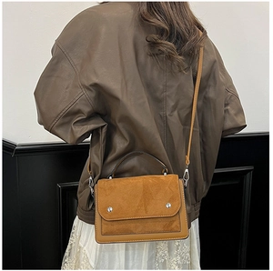 Brown leather crossbody bag with silver rivets shown worn by a model in casual style