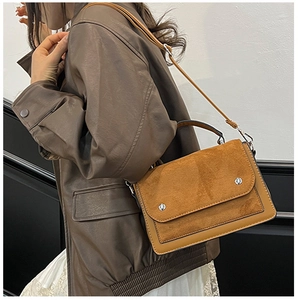Brown leather crossbody bag with suede flap and silver rivets worn by a model