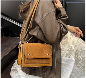 Detail of brown patchwork shoulder bag with matte finish and silver studs worn by model
