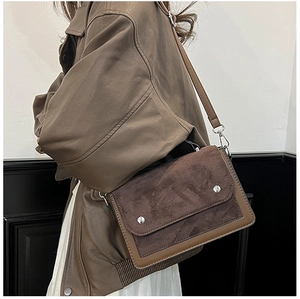Detail of color-block crossbody bag featuring brown suede flap and silver studs on strap