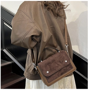 Close-up of contrast brown crossbody bag on model featuring suede flap and metal buckles