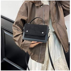 Detail shot of a black leather crossbody bag featuring suede patchwork and silver studs