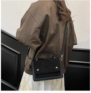 Detail of black contrast stitch bag with silver studs worn by a model in brown leather jacket
