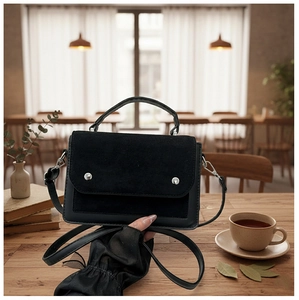 Black suede crossbody bag with silver buckles placed on a cozy cafe wooden table