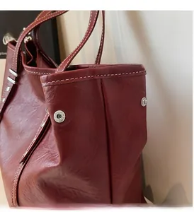 Detail of burgundy leather tote bag with white stitching and silver metal hardware
