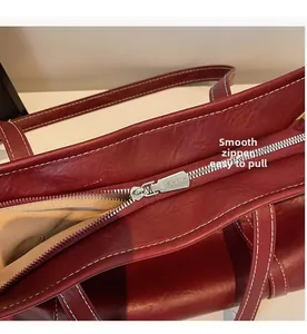 Close-up of silver metal zipper and white contrast stitching on burgundy leather tote