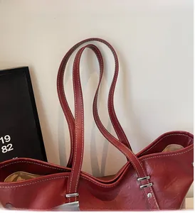 Detail of dark red leather tote bag with white stitching and silver buckles