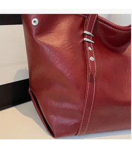 Detailed close-up of dark red tote bag featuring contrast white stitching and silver studs