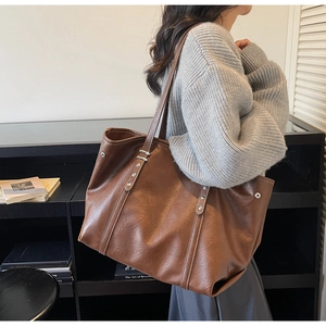 Detail of a brown tote bag featuring silver rivets and white contrast stitching on soft leather