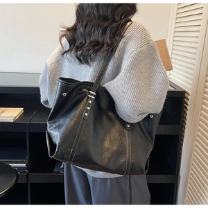 Detail of black tote bag featuring white contrast stitching and metallic rivets