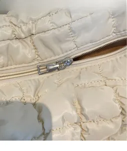 Gros plan sur la fermeture éclair argentée du sac matelassé beige et sa texture fine