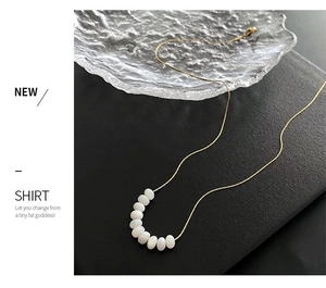 Close-up of gold chain necklace with eight white oval beads and a lobster clasp detail