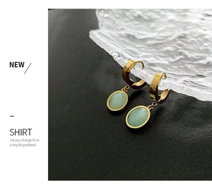 Détail de boucles d'oreilles créoles dorées avec pendentifs ovales verts sur plateau
