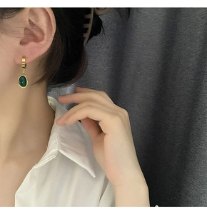 Gros plan de boucles d'oreilles créoles dorées avec zircons verts en forme de larme
