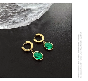Détail de créoles dorées avec pendentifs en forme de goutte en zircon vert émeraude poli