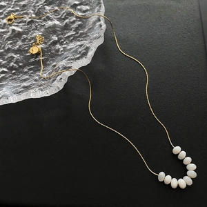 Minimalist gold link necklace featuring nine elegant white pebble beads on a black base