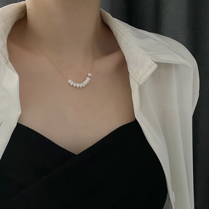 Minimalist gold chain necklace with white beads worn by model on white shirt