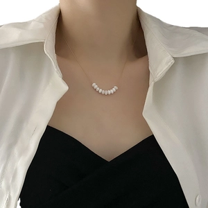 Minimalist gold necklace with nine white pearls on a model wearing white shirt