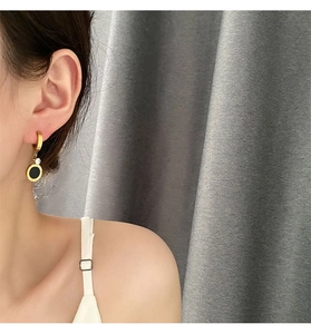 Détail de boucles d'oreilles dorées avec chiffres romains et zircon noir sur mannequin