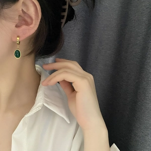 Boucles d'oreilles pendantes dorées avec zircons émeraude portées par un mannequin