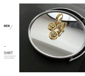 Detail of golden Hamsa Hand earrings with cutout design on a reflective mirror surface