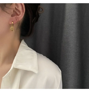 Close-up of a gold Hamsa hand charm earring worn on a model with grey fabric background