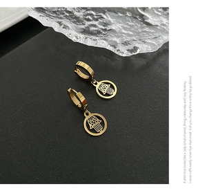 Macro detail of gold Hamsa Hand earrings with hollow geometric design on black background