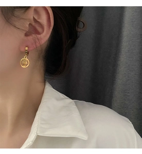 Detailed view of a gold plated Hamsa Hand geometric charm earring worn by a model