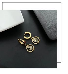 Close-up of gold-plated geometric Hamsa Hand hoop earrings on a textured black surface
