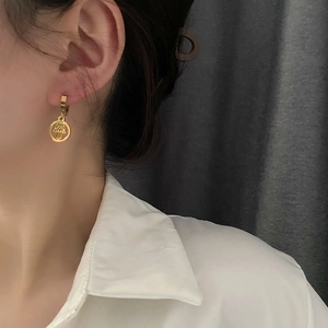 Gold Hamsa Hand charm earrings in hollow geometric design worn by model on white shirt