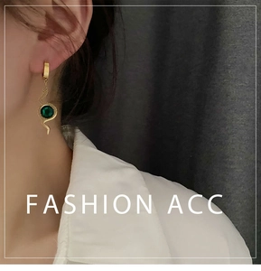 Detail of snake-shaped golden earrings featuring a round emerald green gemstone pendant