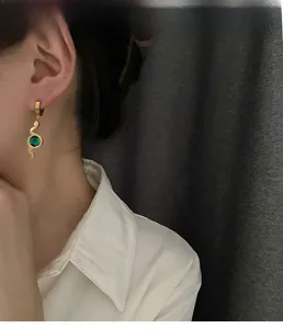 Close-up of golden snake pendant earring with a faceted green zircon on model
