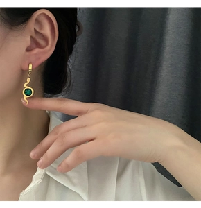 Detailed close-up of a snake-shaped gold earring with a round green zircon on a model