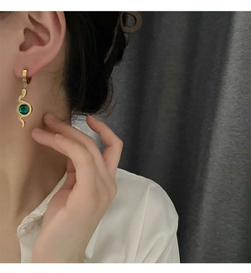 Detail view of gold snake-shaped earrings with green zircon pendant on a model ear