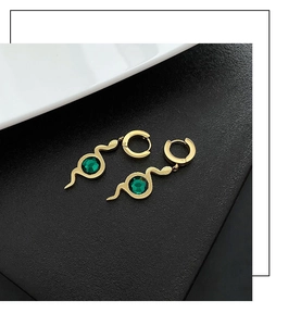 Detail of snake drop earrings with green zircon inlay on textured black background