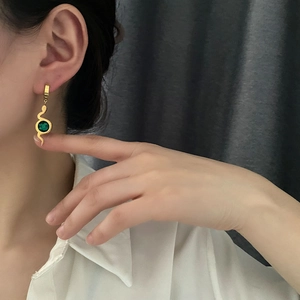 Hammered gold snake earrings with green zircon pendant on a model wearing white shirt
